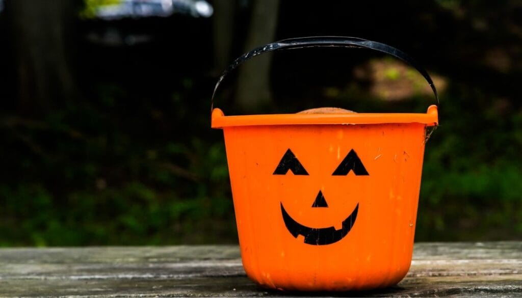 Orange pumpkin bucket with smiling jack-o'-lantern face on wooden table.