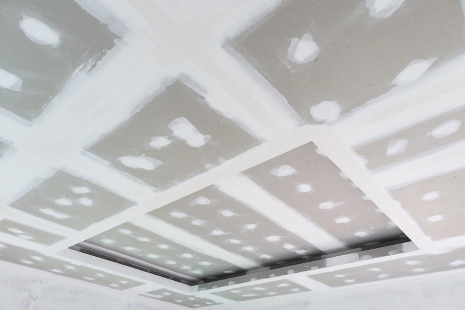 Fire-resistant drywall ceiling panels being installed, with white joint compound applied to the seams and fastener spots.