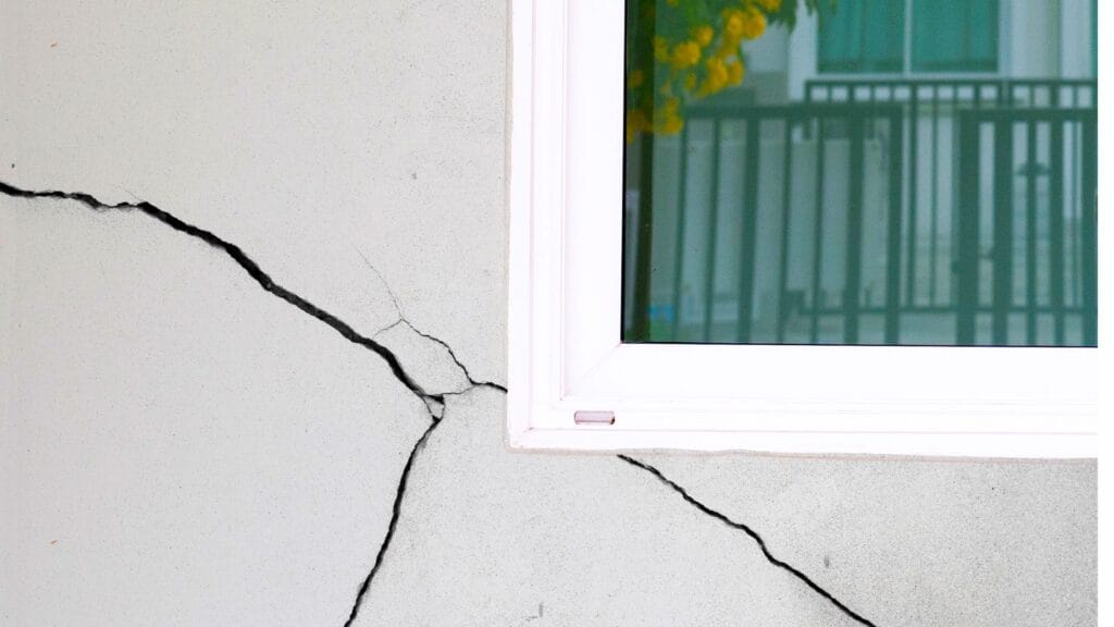 Large, prominent diagonal crack in a white exterior wall near a window frame.