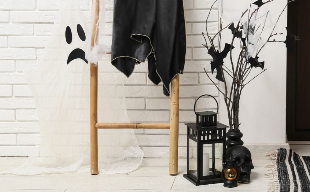 Minimal Halloween decor with ghost, bats, and black lantern by white brick wall.
