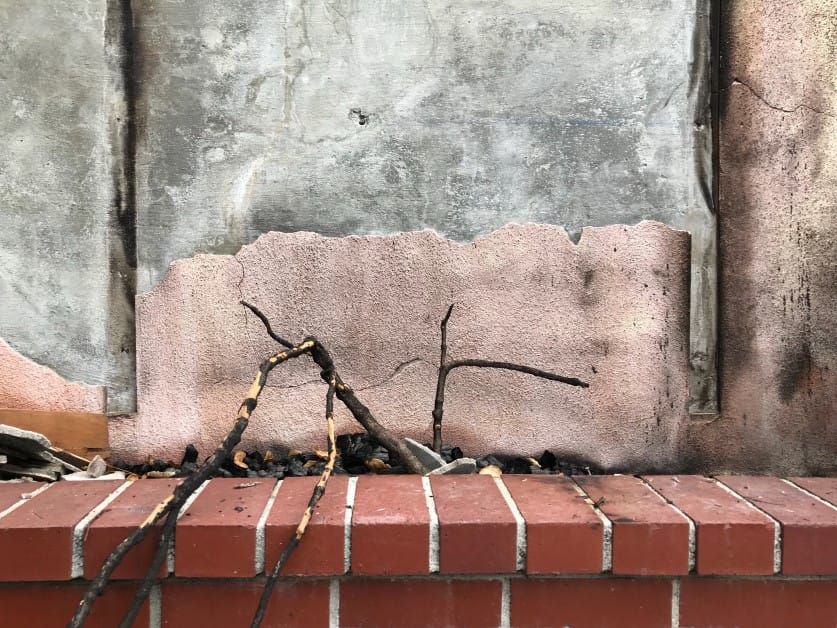Close-up of burnt sticks on red bricks against a smoke-stained wall.