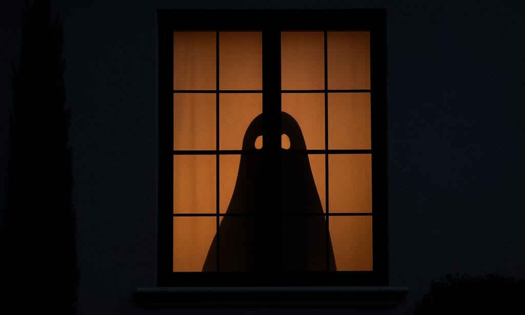 Ghost silhouette in window with orange light background for Halloween.