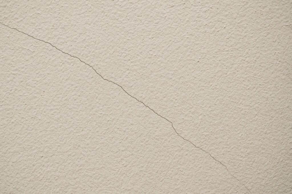 Close-up of a faint, thin hairline crack running diagonally across a textured beige wall.