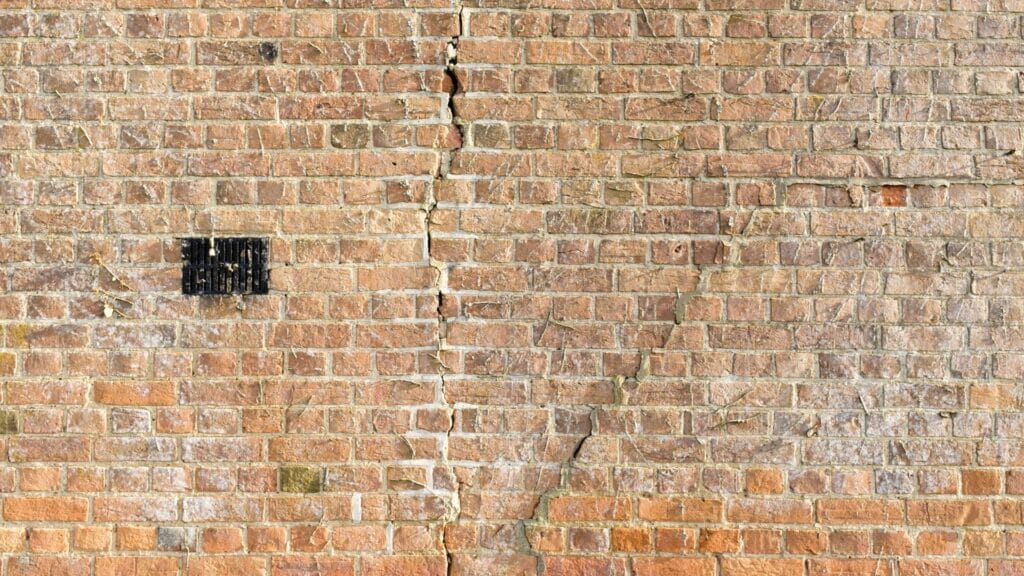 Prominent vertical crack running down the center of an old red brick wall.