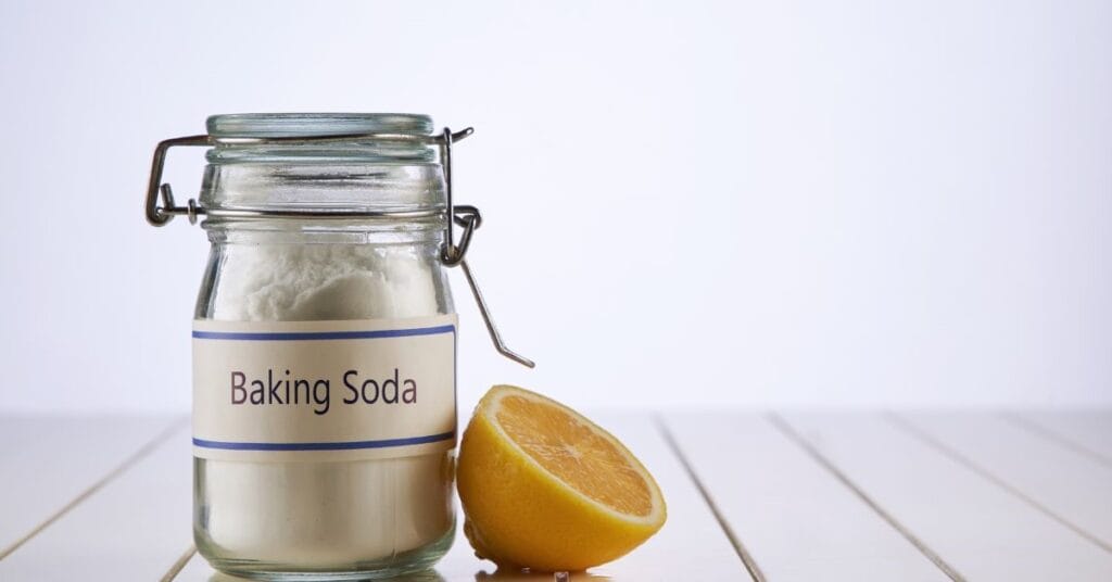 Jar of baking soda next to a half lemon for use as a natural cleaner.