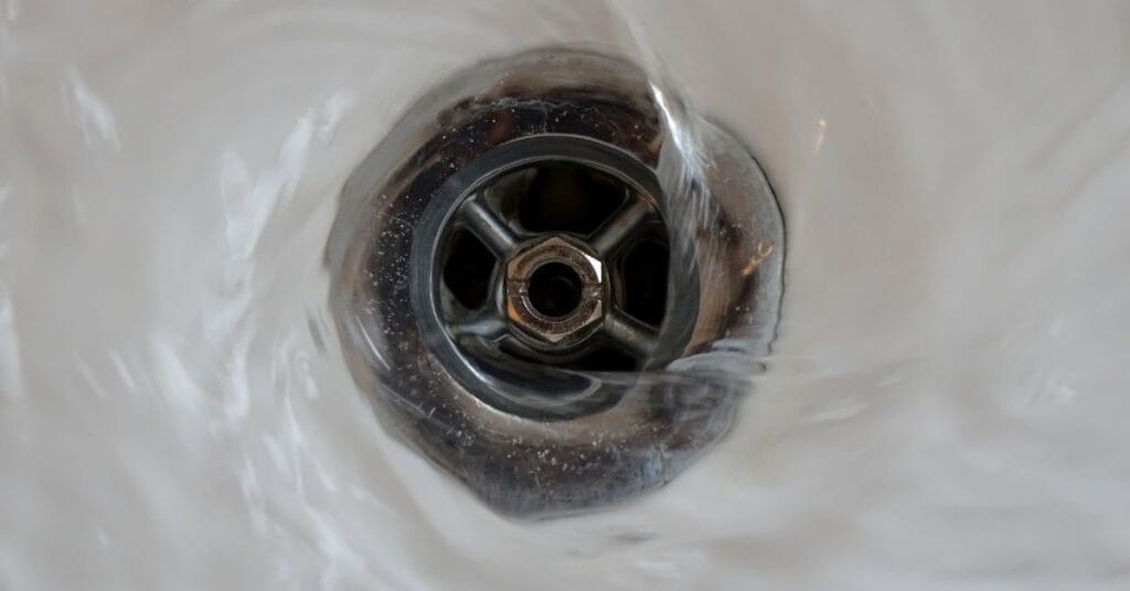 Close view of water swirling down a clean, metal sink drain.