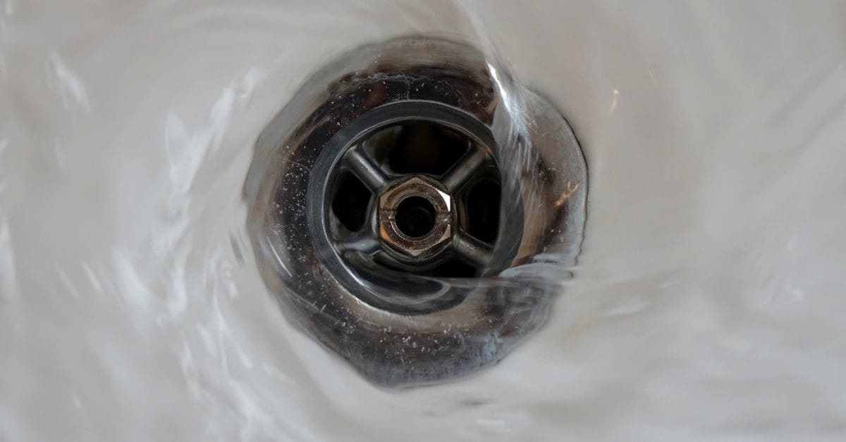 Close view of water swirling down a clean, metal sink drain.
