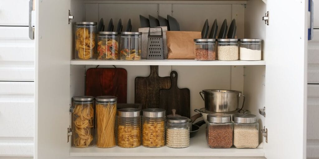 Organized kitchen cupboard with pasta and grains in jars, a great New Year storage habit.