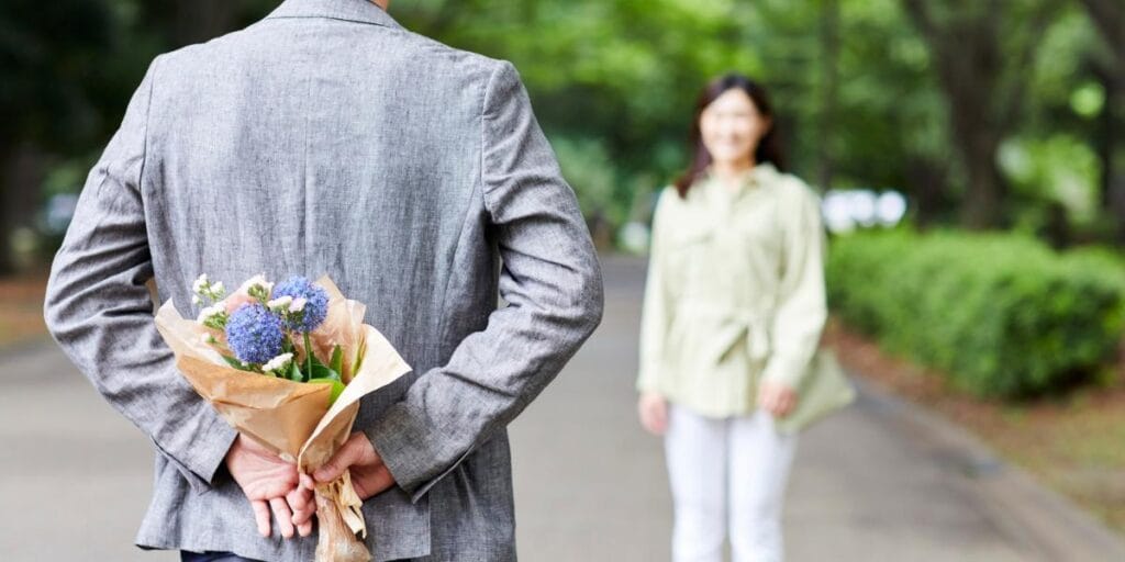 A man hiding a Valentine's day flower bouquet behind his back to surprise a woman.