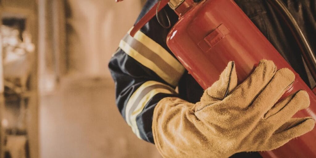 A firefighter in protective gear carrying a red fire extinguisher in a residential setting.
