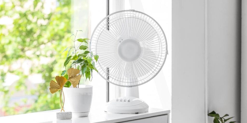 White electric desk fan on a windowsill to cool room without AC