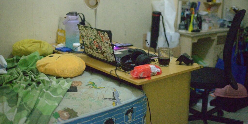Cluttered work desk placed right next to a bed