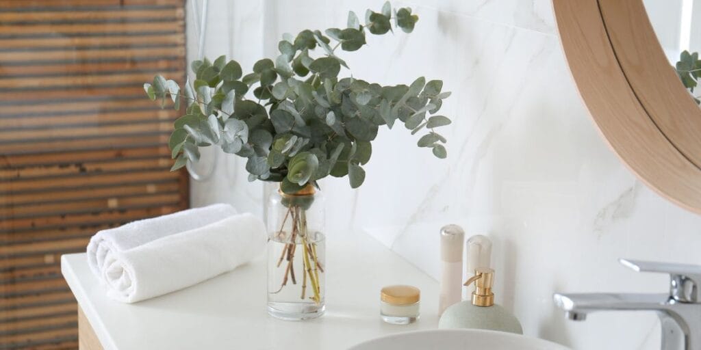 Fresh green eucalyptus branches in a glass vase on a bright white marble bathroom vanity countertop.