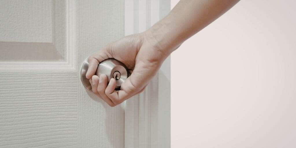 Hand touching a silver door knob, a frequently overlooked surface for household germs.