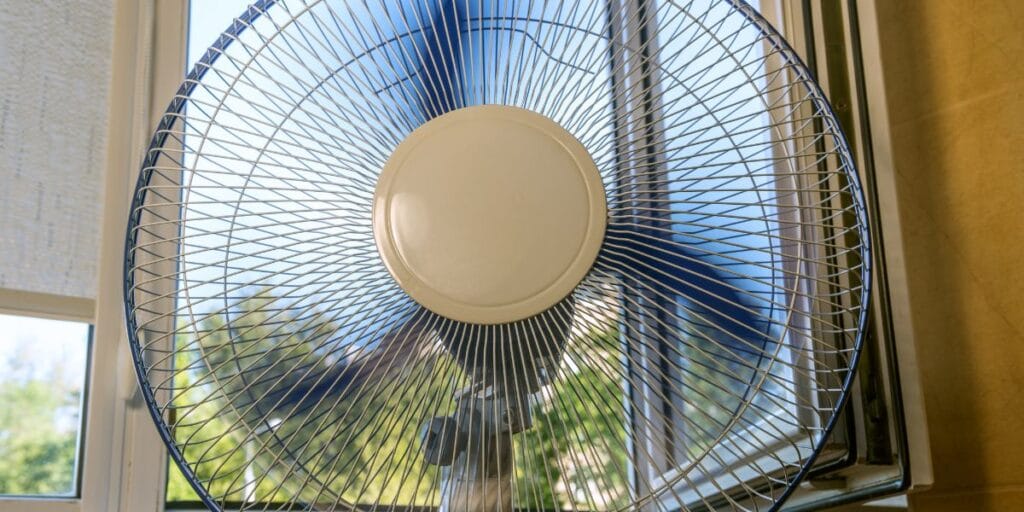 electric fan positioned in front of an open window to circulate cool air in a hot weather