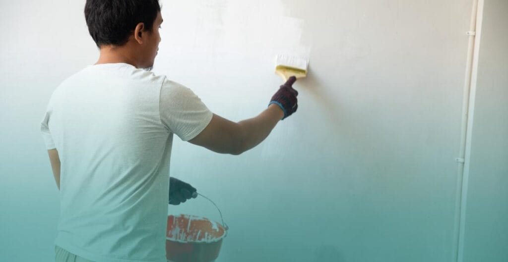 A person uses a brush to paint a white wall, demonstrating a common renter-friendly project to refresh a room's appearance.